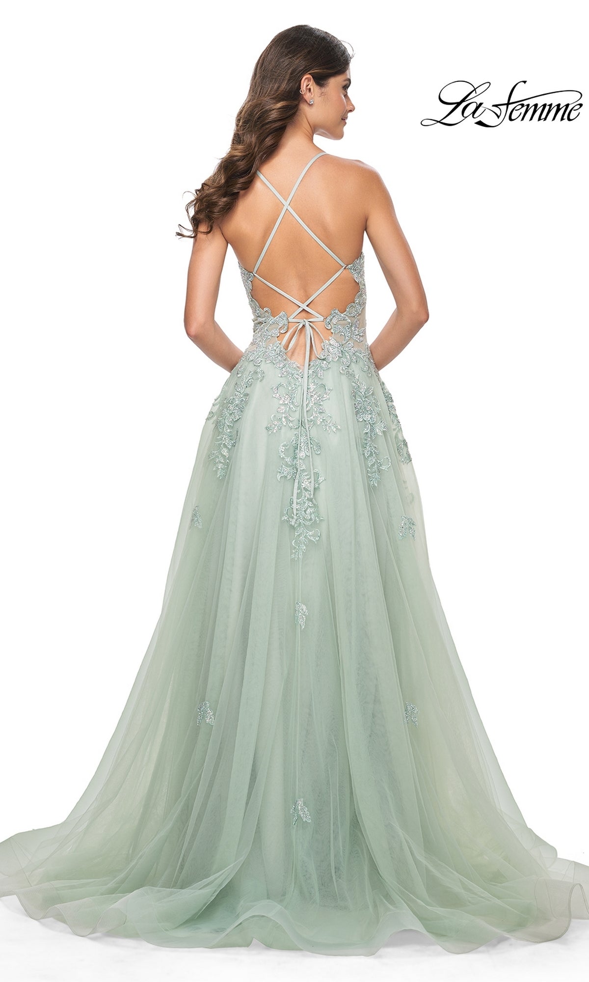 A woman wears the Sheer-Waist Long A-Line Prom Dress (La Femme 32438), a floor-length light green gown with delicate floral embroidery, an open crisscross lace-up back, tulle skirt, and elegant sheer waist detail.